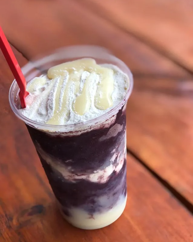 Copo de açaí com camada de creme e leite condensado escorrendo por cima, com colher vermelha