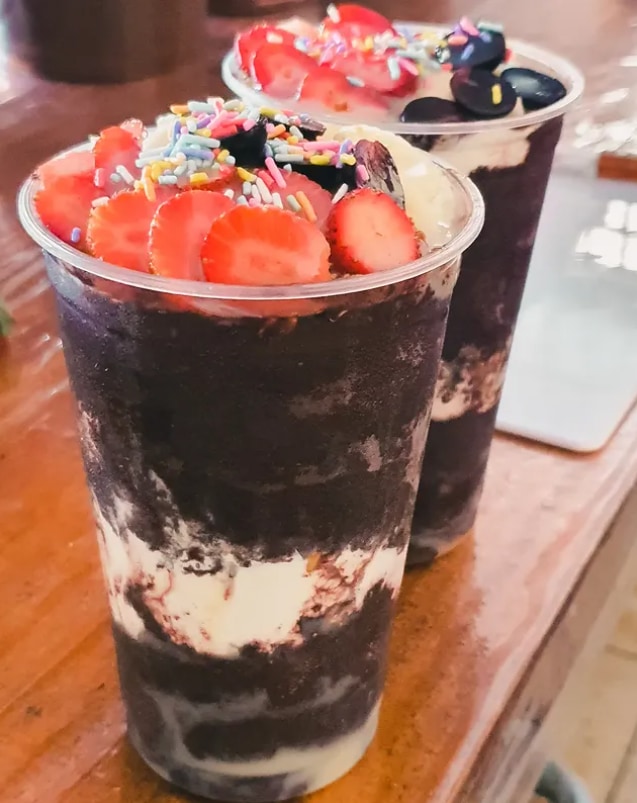 Copos de açaí cobertos com fatias de morango, confeitos coloridos e discos de chocolate