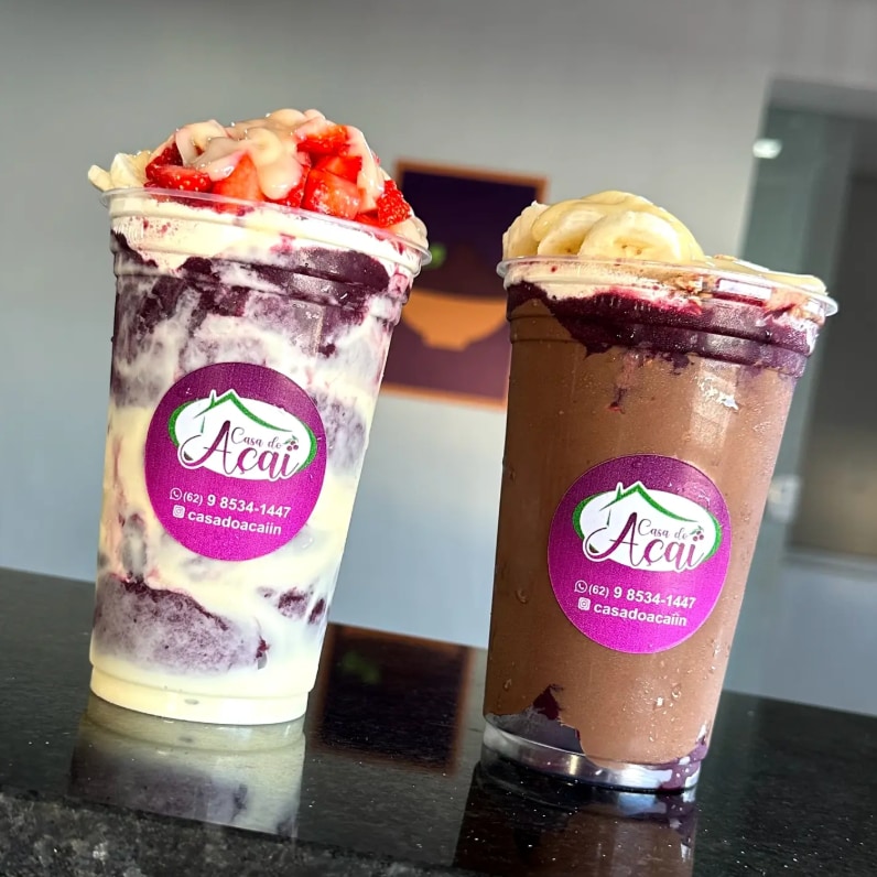 Dois copos de açaí com o adesivo da casa, um com morango e outro com banana e creme