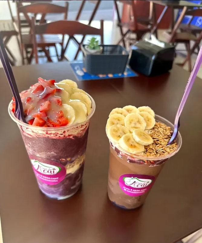 Dois copos de açaí sobre mesa de madeira, um com morango e banana, outro com banana e granola