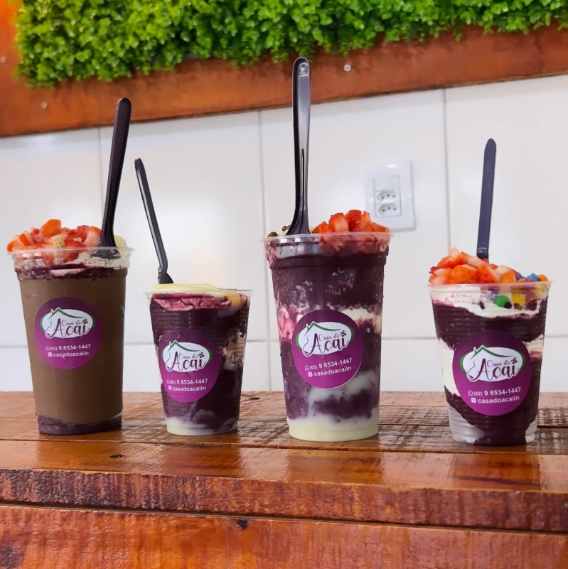 Quatro copos de açaí de tamanhos diferentes enfileirados no balcão de madeira