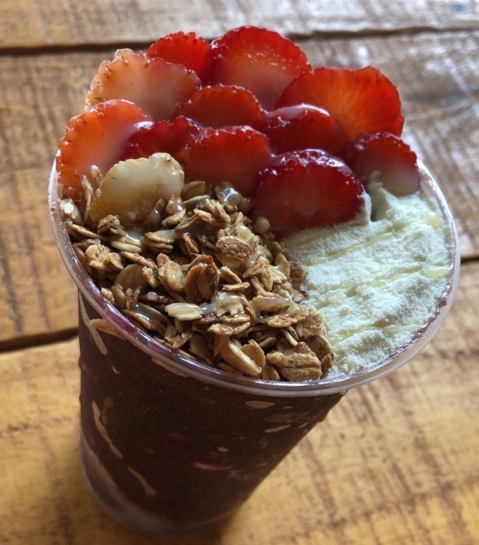 Tigela de açaí vista de cima com morangos fatiados, granola e creme branco